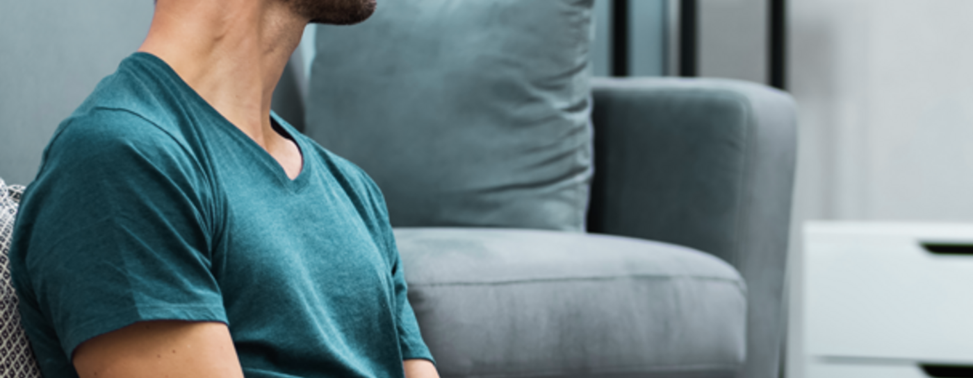 Mann sitzt auf dem Fußboden, mit dem Rücken ans Sofa gelehnt, hat ein I-Pad in der Hand und schaut linksseitig auf einen Fernseher, der auf einem weißen Sideboard steht. Auf dem Bildschirm vom TV steht: Volle Fernseh-Vielfalt mit waiputv.