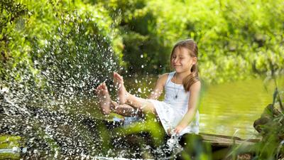 Mädchen spielt mit Wasser an einem Bach im Wald.