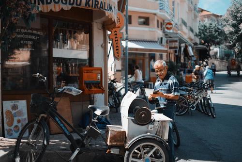 Älterer Herr mit Brille und T-Shirt steht an einer Straßenecke in einer türkischen Stadt vor einem Laden im Sonnenschein