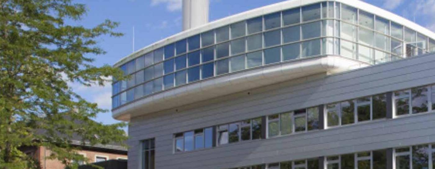 Silbernes Gebäude mit breiter Fensterfront. Davor ein voller Parkplatz.
