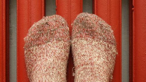 Füße mit dicken Socken werden zum Aufwärmen an die rote Heizung gedrückt.