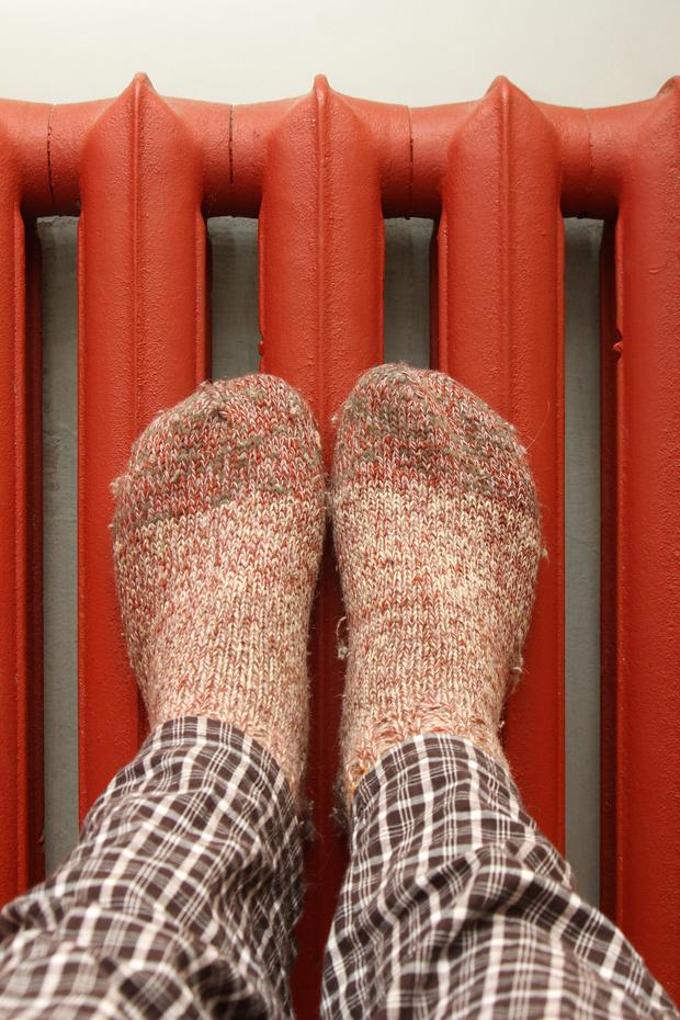 Füße mit dicken Socken werden zum Aufwärmen an die rote Heizung gedrückt.