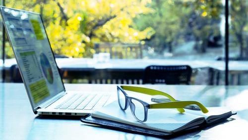 Aufgeklappter Laptop mit Glasfaser-Anschluss der Stadtwerke Flensburg steht im Freien auf einem Tisch, davor liegt eine Brille auf einem Buch