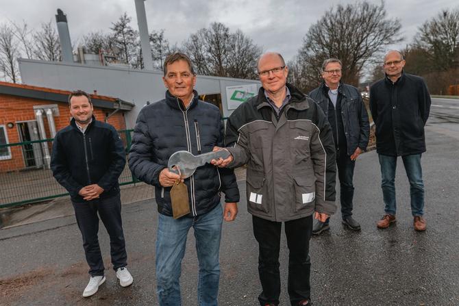 5 Männer stehen freundlich schauend vor dem Heizkraftwerk in Langballig. Die zwei mittig stehenden halten einen sehr großen Schlüssel in den Händen.