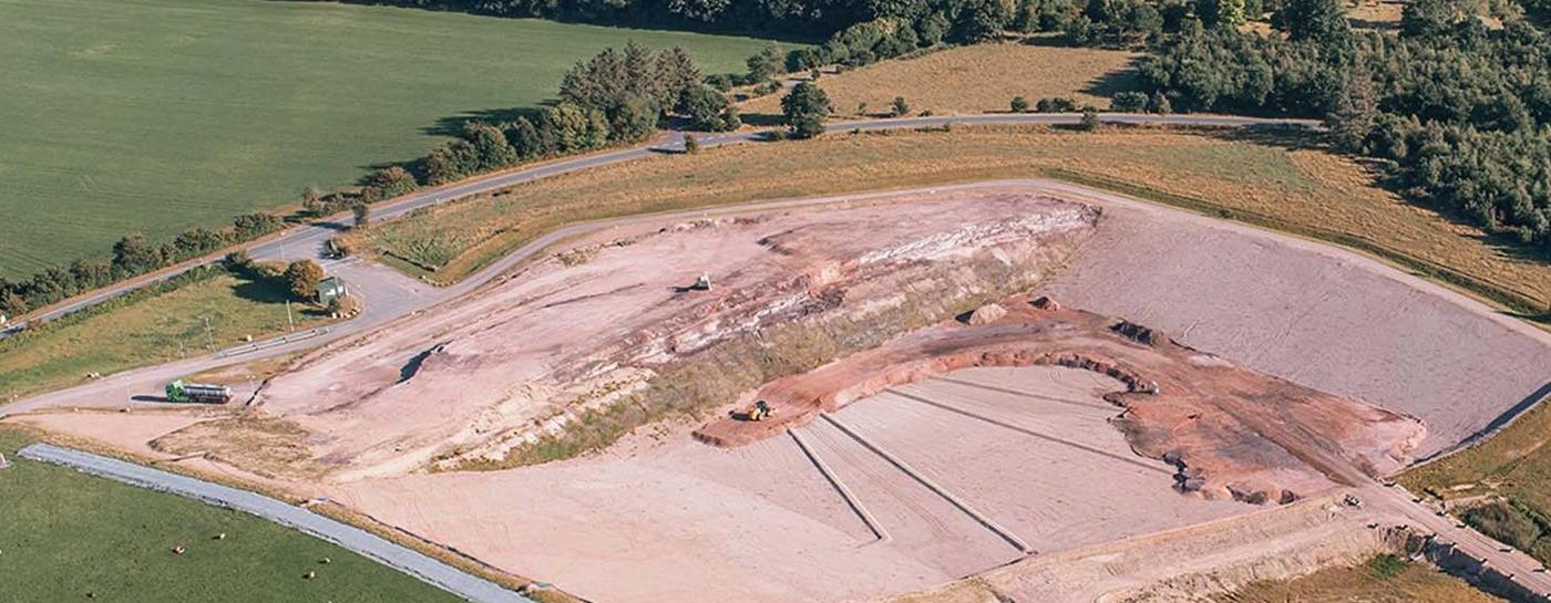 Von oben Perspektive einer Deponie mit Sand- und Grasflächen sowie einem Wasserbecken.
