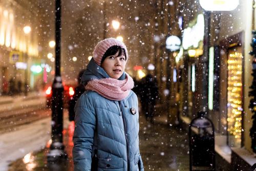 Frau in Winterjacke, Schalt und Mütze steht an einer Straße im Schneegestöber