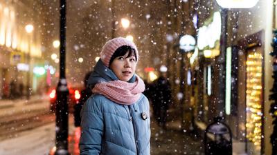 Frau in Winterjacke, Schalt und Mütze steht an einer Straße im Schneegestöber