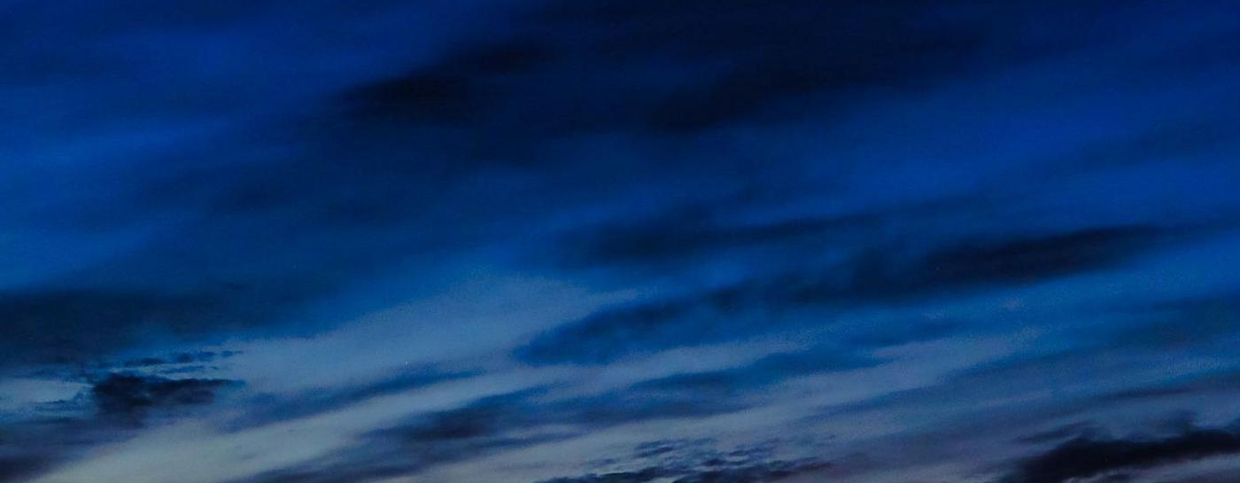 Stadtwerke bei Nacht von der Wasserseite aus fotografiert. Lichter der Gebäude spiegeln sich im Wasser und der Himmel erleuchtet in dunklem Blau und orange durch die Wolken.
