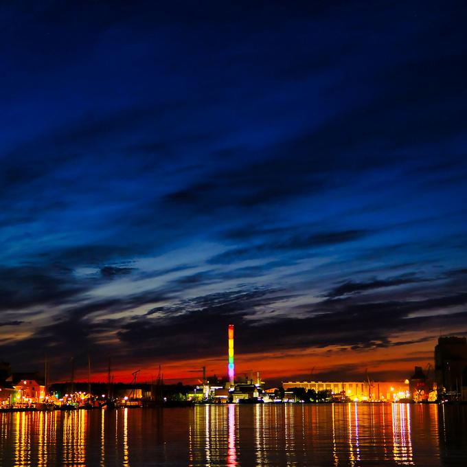 Stadtwerke bei Nacht von der Wasserseite aus fotografiert. Lichter der Gebäude spiegeln sich im Wasser und der Himmel erleuchtet in dunklem Blau und orange durch die Wolken.