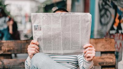 Zwei Hände halten in Nahaufnahme eine Zeitung in der Hand. Der Text ist lesbar.