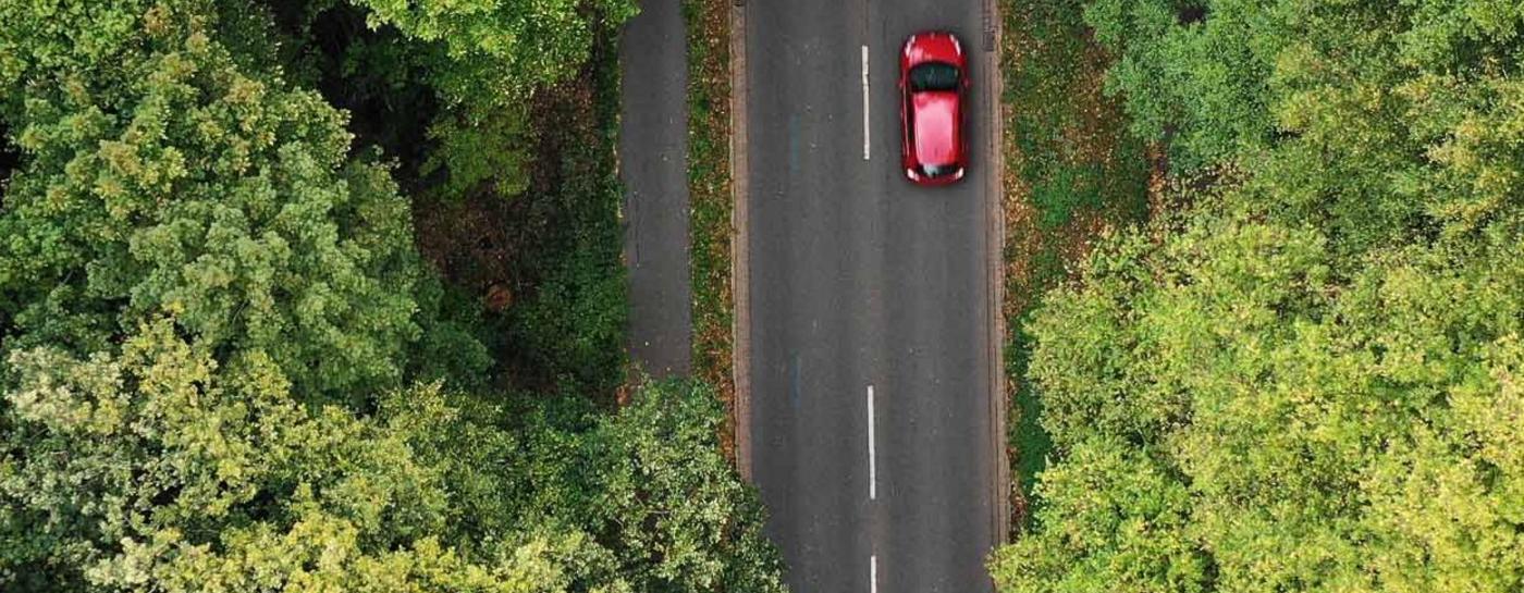 E-Auto fährt auf einer Landstraße. Links und rechts neben der Straße sind viele grüne Baumkronen von oben zu sehen.
