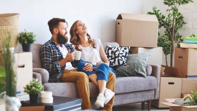 Junges Paar entspannt sich in mitten Umzugskartons mit einem Kaffe auf dem Sofa. 