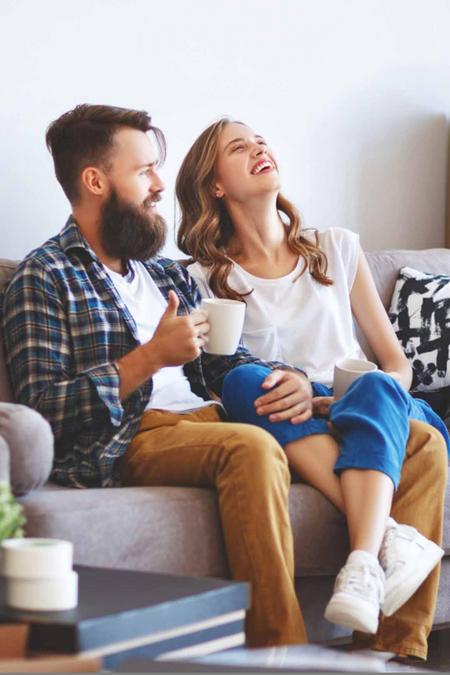 Junges Paar entspannt sich in mitten Umzugskartons mit einem Kaffe auf dem Sofa.