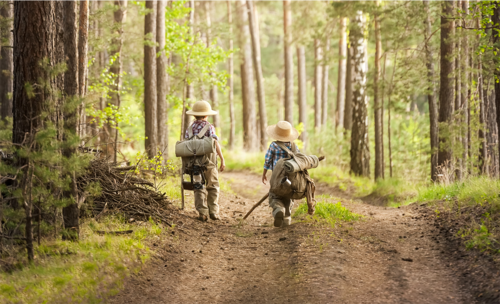 Zwei Kinder in traditioneller Wanderkleidung gehen durch einen Laubwald.