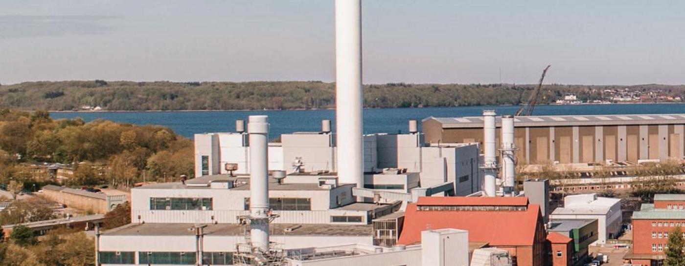Gelände der Stadtwerke Flensburg von oben fotografiert bei Sonnenschein und klarem Himmel und ruhiger Förde. Auf dem Wasser sind Schiffe.