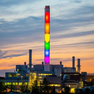 Der Schornstein der Stadtwerke Flensburg leuchtet in Regenbogenfarben bei Dämmerung.