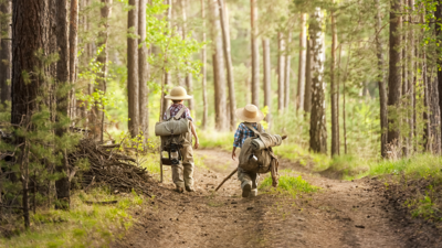 Zwei Kinder in traditioneller Wanderkleidung gehen durch einen Laubwald.