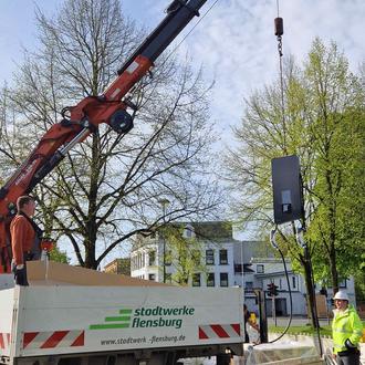 Ein roter Kran hebt eine Ladesäule von einem Lastwagen der Stadtwerke Flensburg herunter.