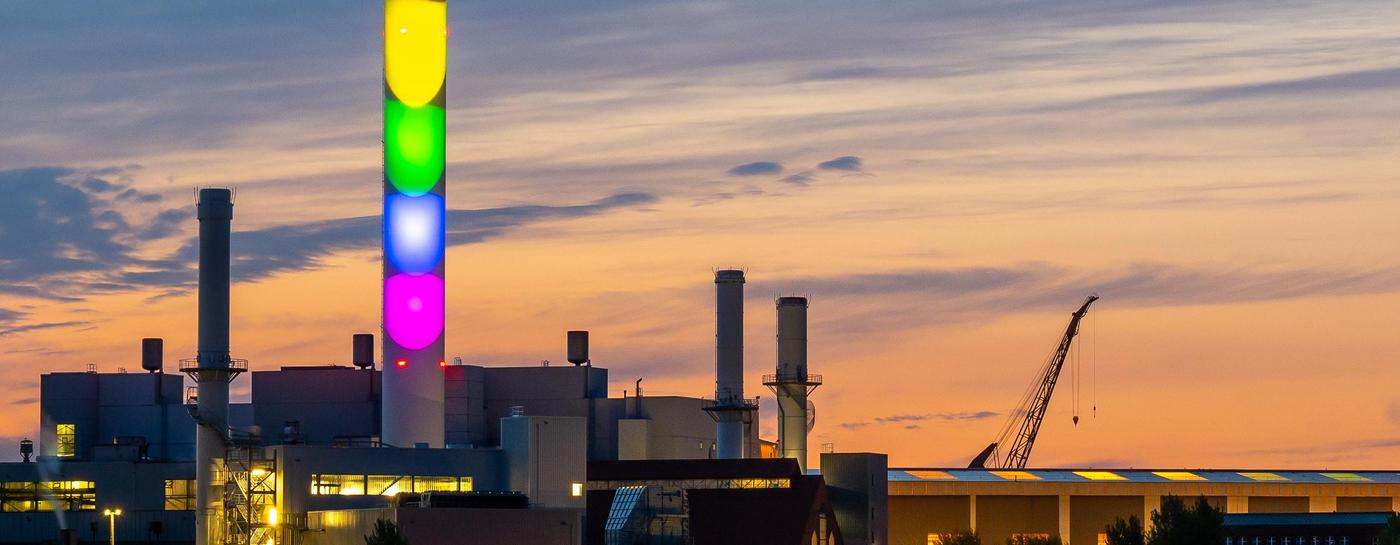 Stadtwerke Flensburg Schornstein in Regenbogenfarben beleuchtet bei Dämmerung.