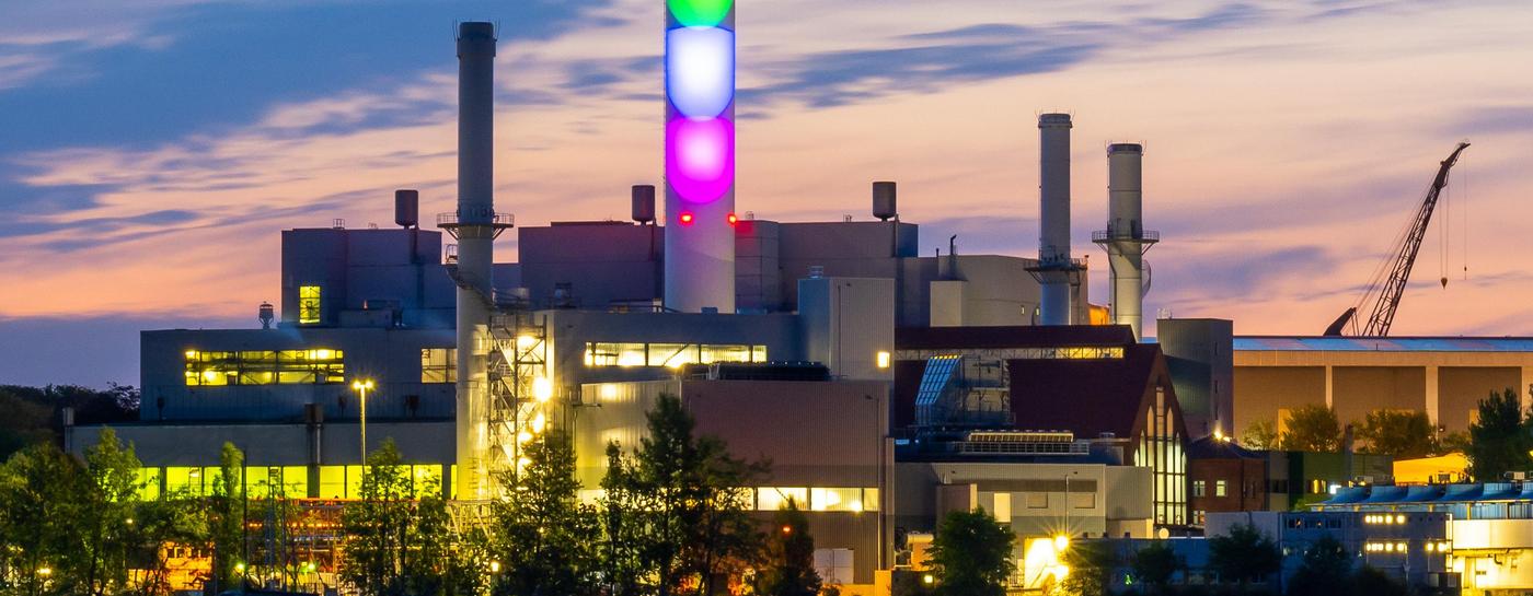 Der Schornstein der Stadtwerke Flensburg leuchtet in Regenbogenfarben bei Dämmerung.