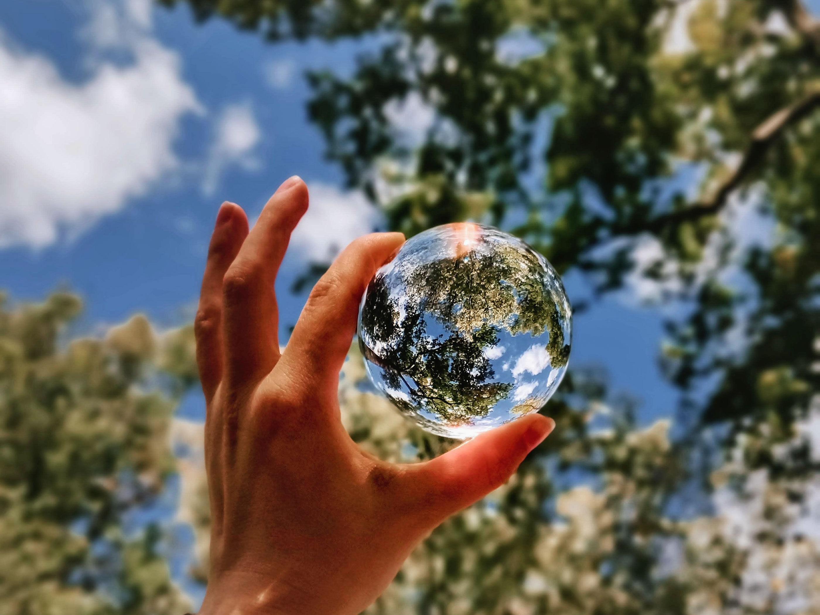 Hand hält Glaskugel in den Himmel