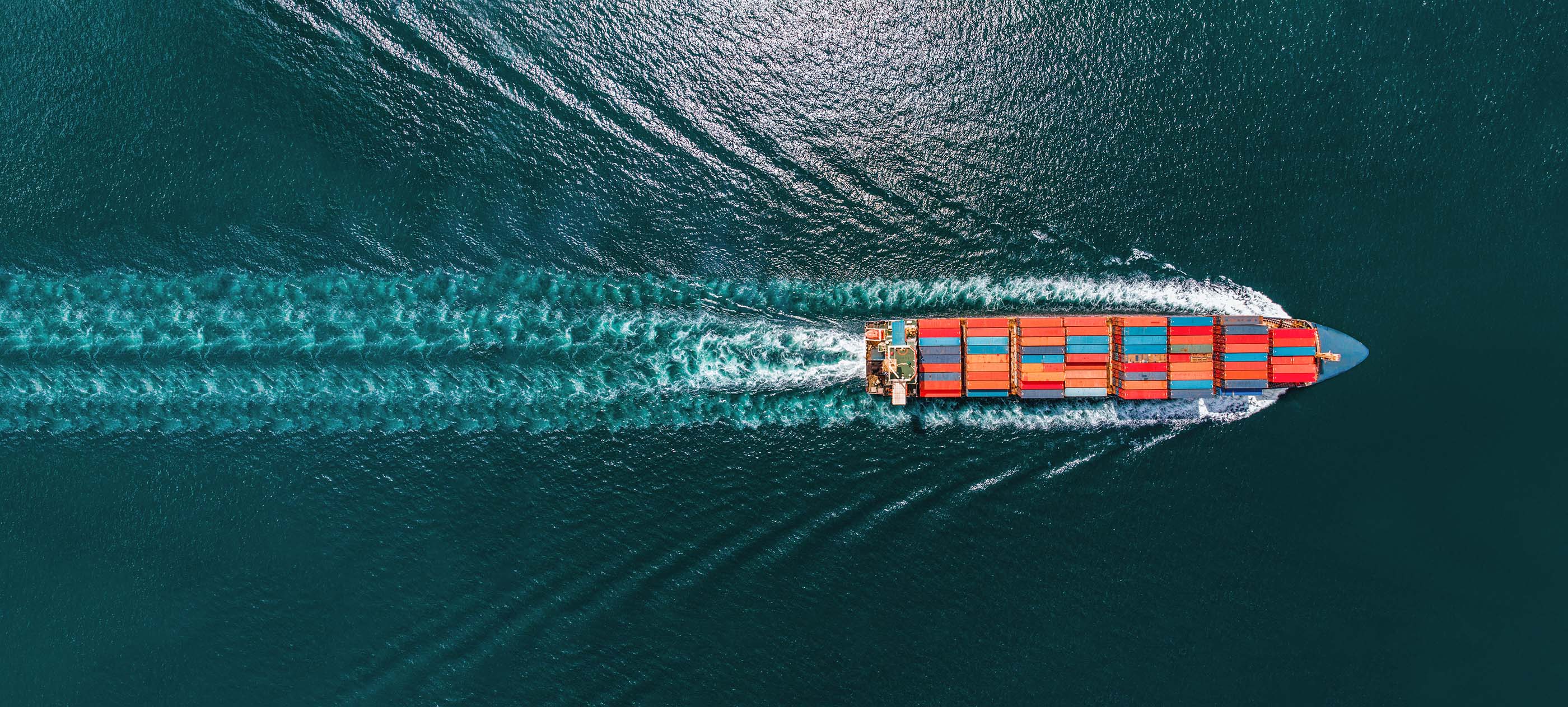 Ein großes blaues Containerschiff mit bunter Beladung, dunkles Wasser mit Wellengang.